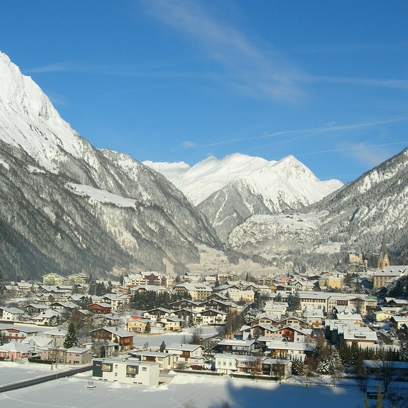 Blick auf die Gemeinde Matrei in Osttirol mit schneebedeckten Dächern und Berggipfeln, an einem herrlichen Wintertag.