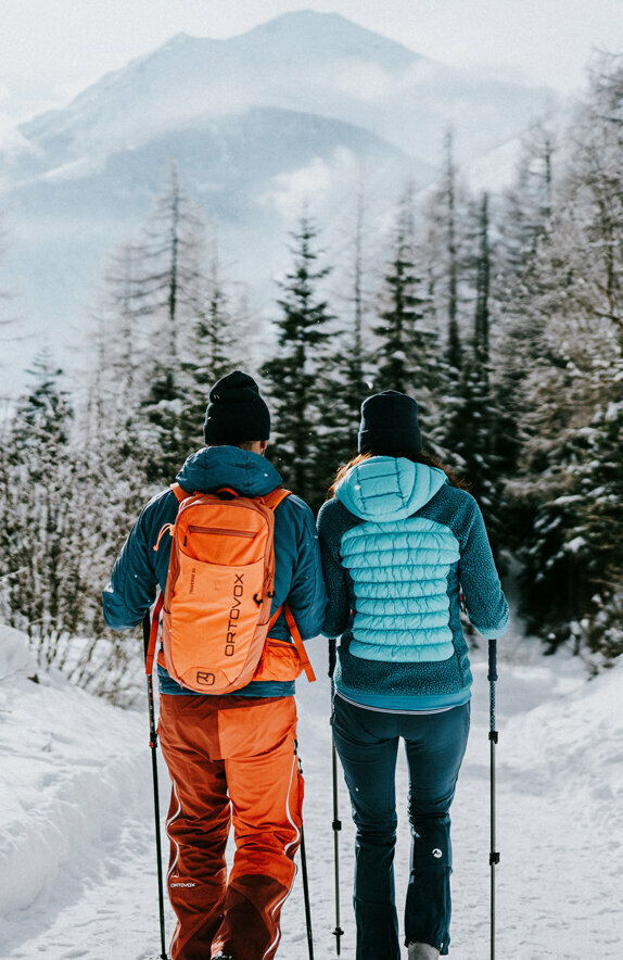 Osttirols Winterwanderwege führen durch ruhige Wälder und eine winterliche Schneelandschaft. Ein Paar beim Winterwandern durch die winterliche Landschaft von Kals am Großglockner