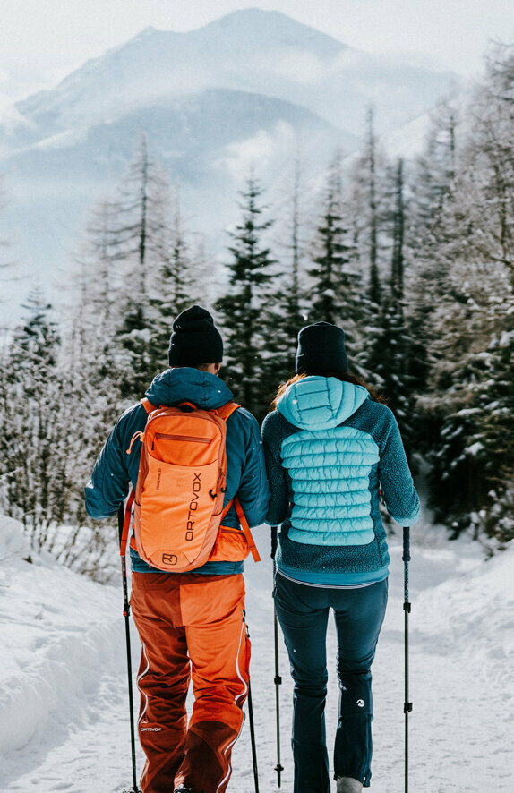 Osttirols Winterwanderwege führen durch ruhige Wälder und eine winterliche Schneelandschaft. Ein Paar beim Winterwandern durch die winterliche Landschaft von Kals am Großglockner
