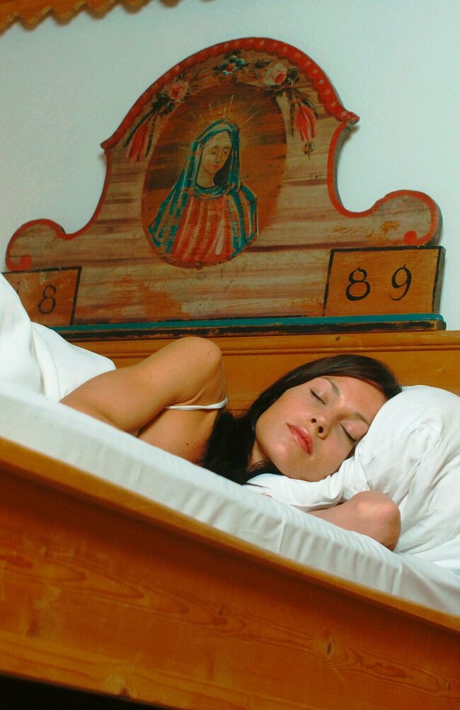 Unterkunft Osttirol Eine Frau schläft in einem Bett mit weißem Bettbezug aus der Ameisenperspektive.