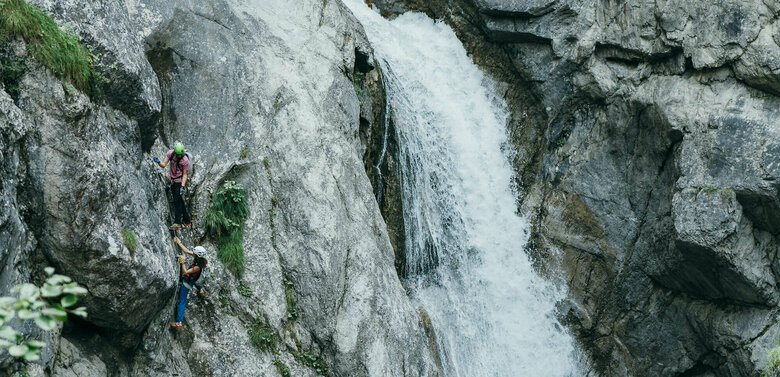 Galitzenklamm Klettersteig Zwei Personen auf einem Klettersteig neben einem Wasserfall in der Galitzenklamm.