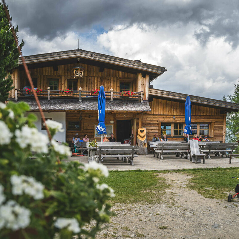 Leckfeldalm Blick auf die urige Leckfeldalm, mit Gaesten auf der Terrasse.