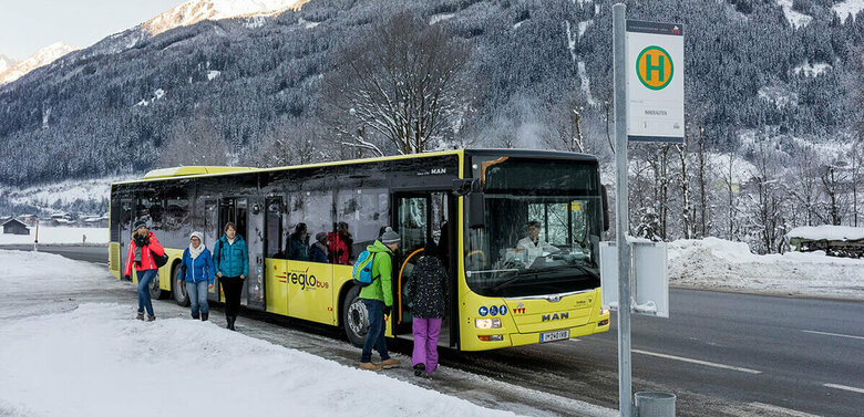 Bus Winter Gelber Bus hält an einer Bushaltestelle im Winter und lässt Fahrgäste ein- und aussteigen.