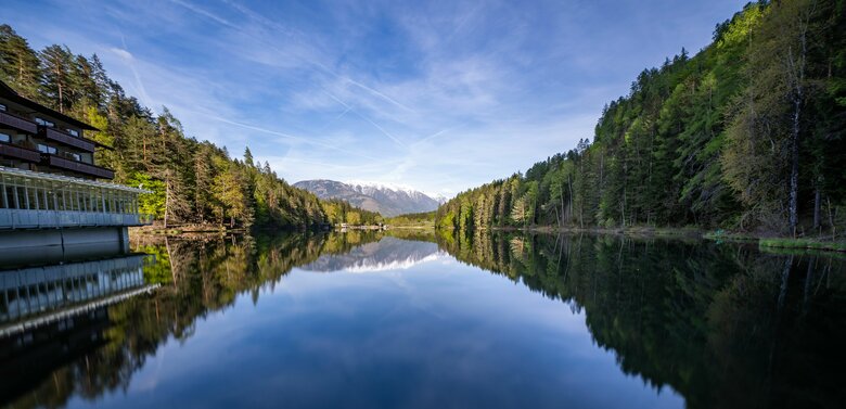 Blick vom Hotel am Tristachersee auf den glasklaren See. Die Bäume spiegeln sich am Rande im Wasser.