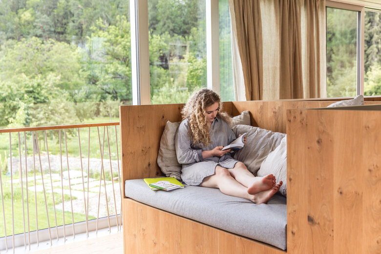 Ruheort Iselhof Frau entspannt auf dem Sofa in ihrer Unterkunft und blättert in einem Buch.