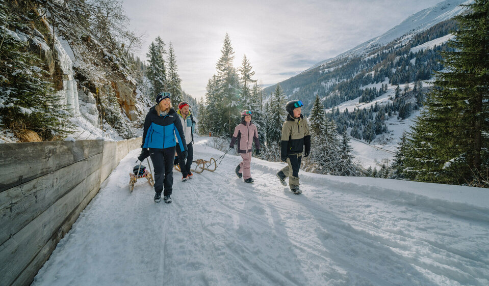 Eine Familie in Schianzügen unterwegs auf der Rodelbahn im verschneiten Winkeltal in Außervillgraten, Osttirol.