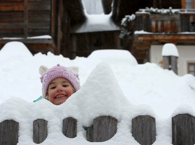 Spielplatz Schnee Ein Kind spielt im tiefen Schnee und schaut grinsend aus dem Schnee.