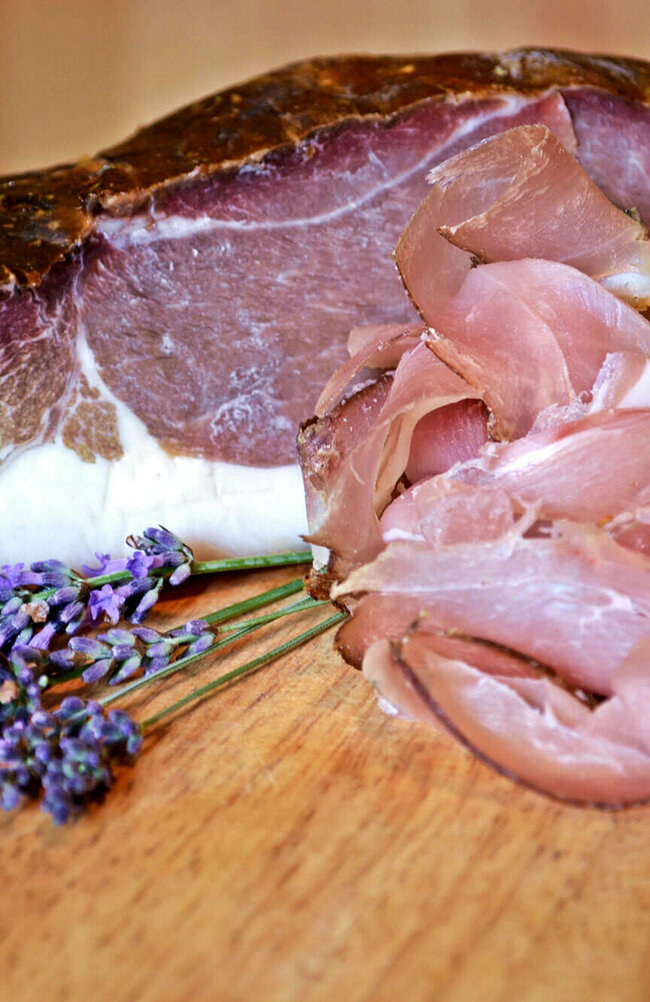 Speck Ein großes Stück Speck mit ein paar dünnen Scheiben geschnittenem Speck und Lavendel.