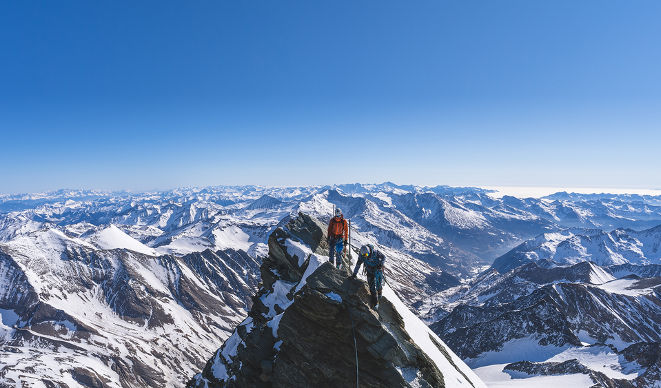 Zwei Alpinisten stehen auf einem hohen Gipfel in Osttirol, ringsherum gibt es zahllose andere Gipfel.