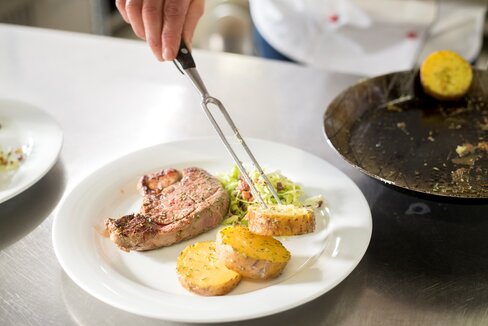 Lenzingerhof Anrichten von einem Stück Fleisch und dicke Kartoffelscheiben mit Krautsalat auf einem weißen Teller auf demLenzingerhof.
