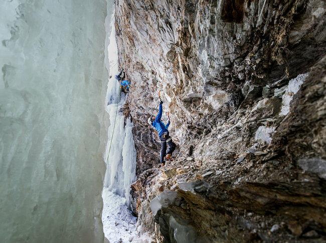 Eiskletterpark Osttirol Kletterer klettern auf einem Felsen neben einem zugefrorenen Wasserfall.