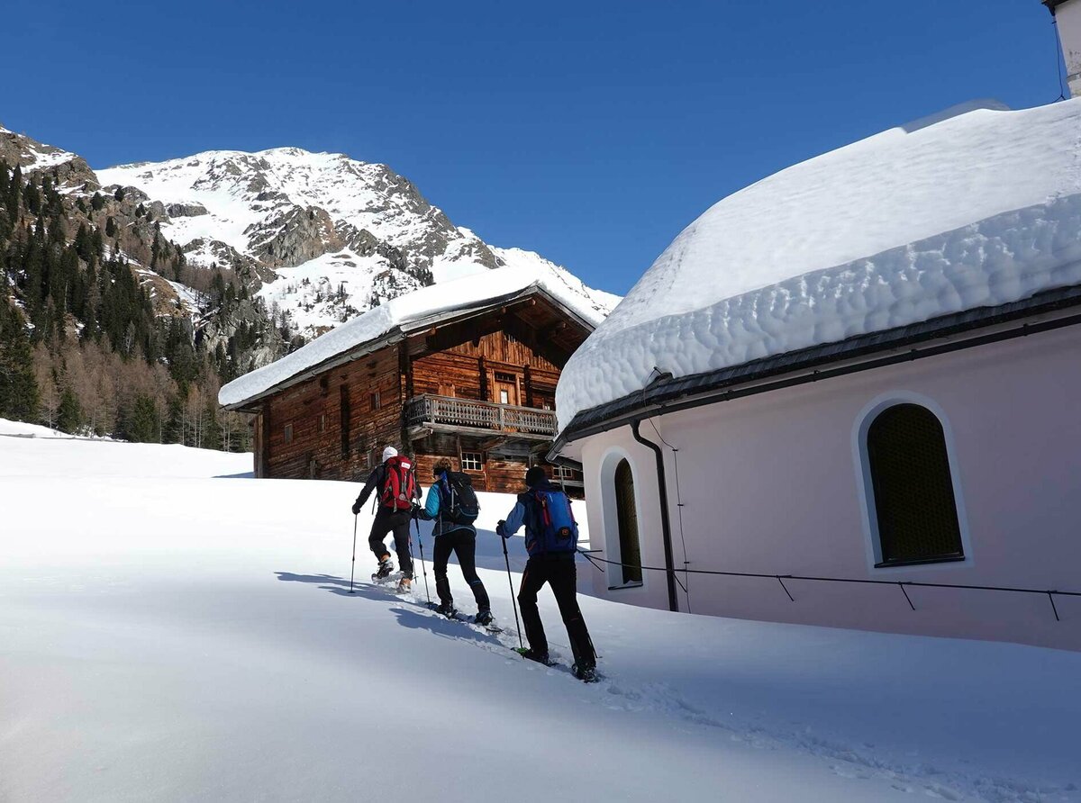 Eine Gruppe beim Schneeschuhwandern, vorbei an einer Kirche im Villgratental