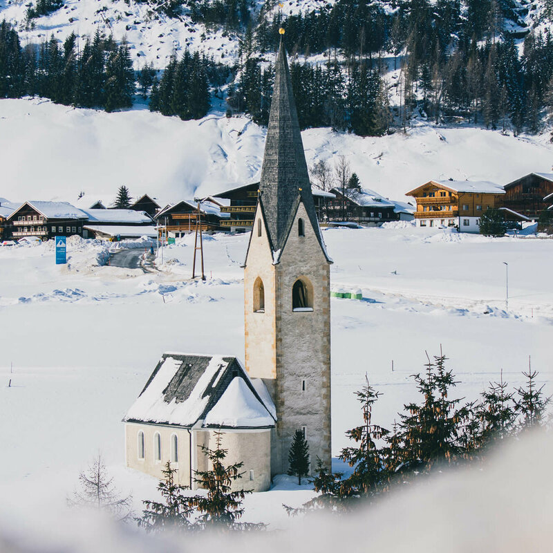 Kals Kirche Die Kals Kirche mit dunklem Kirchturm liegt von Schnee bedeckt vor dem Dorf.