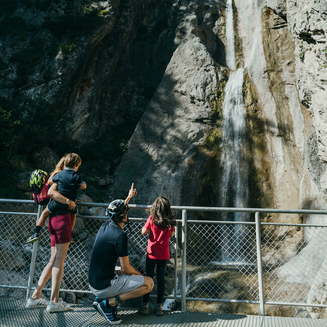 Frauenbach Wasserfall Lavant Eine vierköpfige Familie steht auf der Plattform des Frauenbachwasserfalls in Lavant. Ein Rundwanderweg, auch "Waldpfad" genannt, führt direkt an diesem Naturjuwel vorbei.