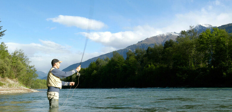 Fliegen fischen Ein Mann steht in einem Fluss und wirft seine Angel aus zum Fliegen fischen.
