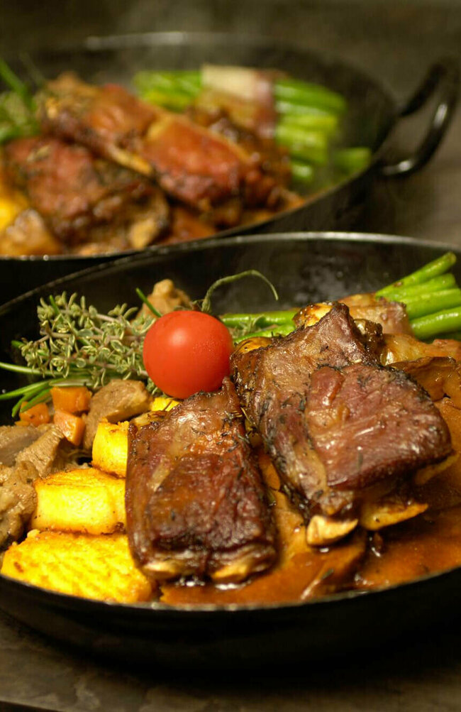 Osttiroler Berglamm Osttiroler Berglamm mit Speckbohnen und Polenta in einem Eisenpfännchen.
