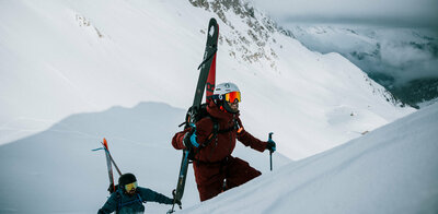 Zwei Skitourengeher befinden sich in einem Steilhang auf ihrer Skitour im Defereggental. Sie tragen ihre Tourenski am Rücken und blicken ihrem Ziel motiviert entgegen.