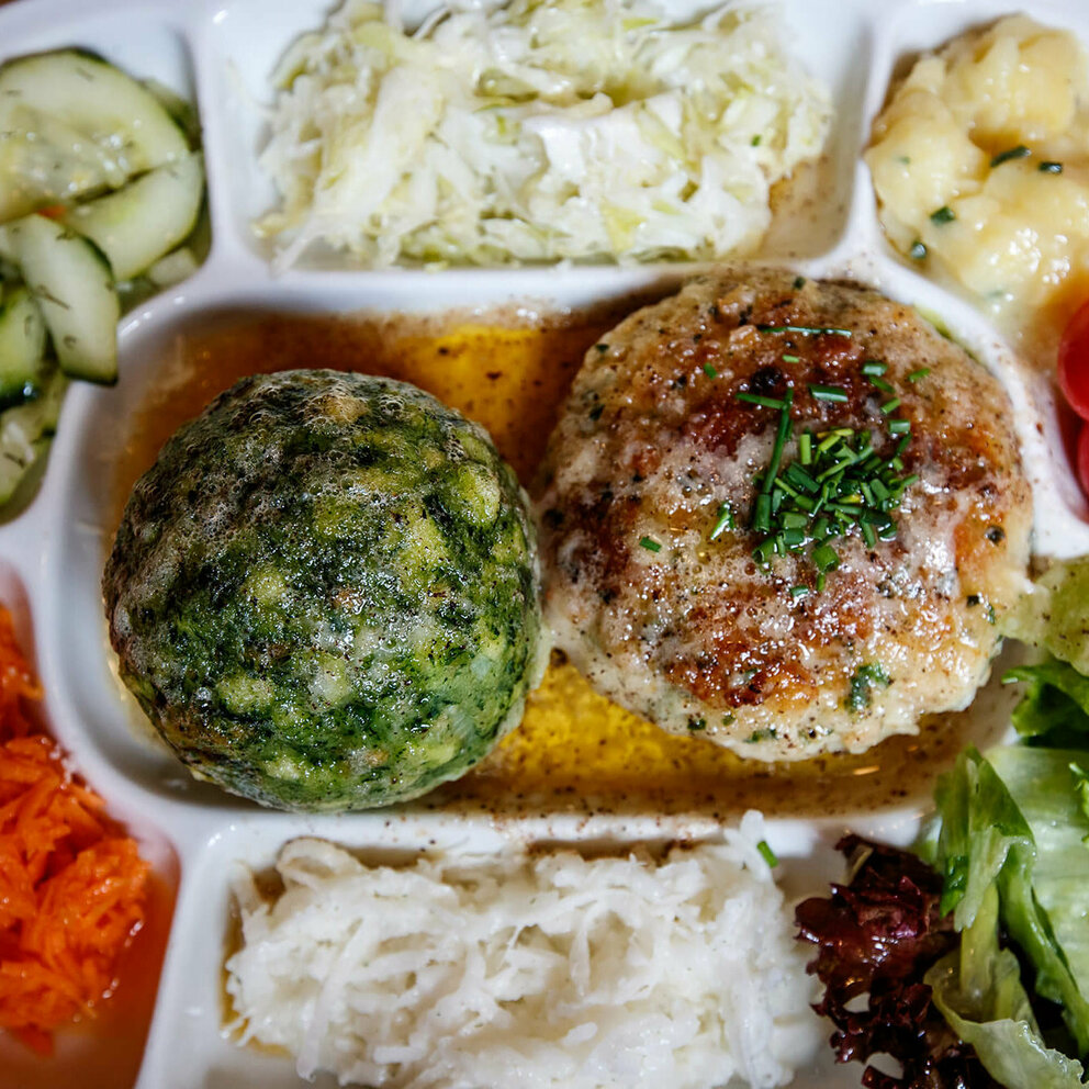 Knödel Spinatknödel und Kaspressknödel in brauner Butter. Ringsherum verschiedene bunte Salate auf einem Teller angerichet.