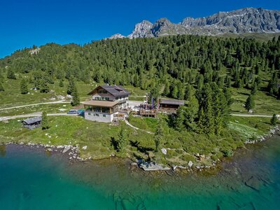 Alpengasthaus Obersee Das Alpengasthaus Obersee im Sommer mit dem darunterliegenden blau-grünen Seeufer am Staller Sattel. Im Hintergrund ist der dichte grüne Wald, der strahlendblaue Himmel und das beeindruckende Bergpanorama zu sehen.