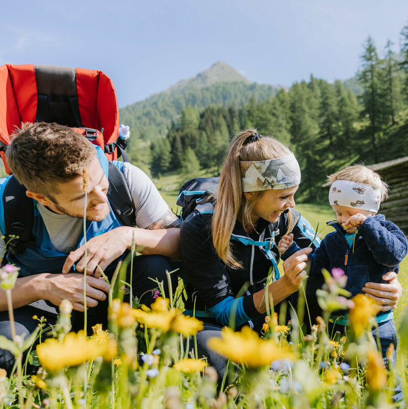 Wiese Familienwanderung Kristeinertal Eine kleine Familie ist im Zuge einer Familienwanderung auf einer Wiese im Kristeinertal. Die Frau und das Kind tragen Stirnbänder und der Mann hat einen roten Trage-rucksack auf dem Rücken. Sie sitzen im grünen Gras.
