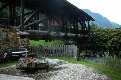 Wasserruheplatz Blosbrücke Der Wasserruheplatz bei der Blosbrücke in Hopfgarten in Defereggen in den Sommermonaten. Das grüne Gras bedeckt das Ufer neben der blauen Schwarzach, über welche die robuste Holzbrücke ragt.