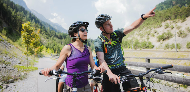 Drauradweg Ein Pärchen in Sportkleidung mit Fahrrädern auf dem Drauradweg. Der Mann zeigt mit dem Finger in die Ferne.