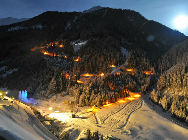 Rodelbahn Tilliachalmweg Die beleuchtete Rodelbahn Tilliachalmweg schlängelt sich in verschneiten Außervillgraten bei Nacht durch den Wald..