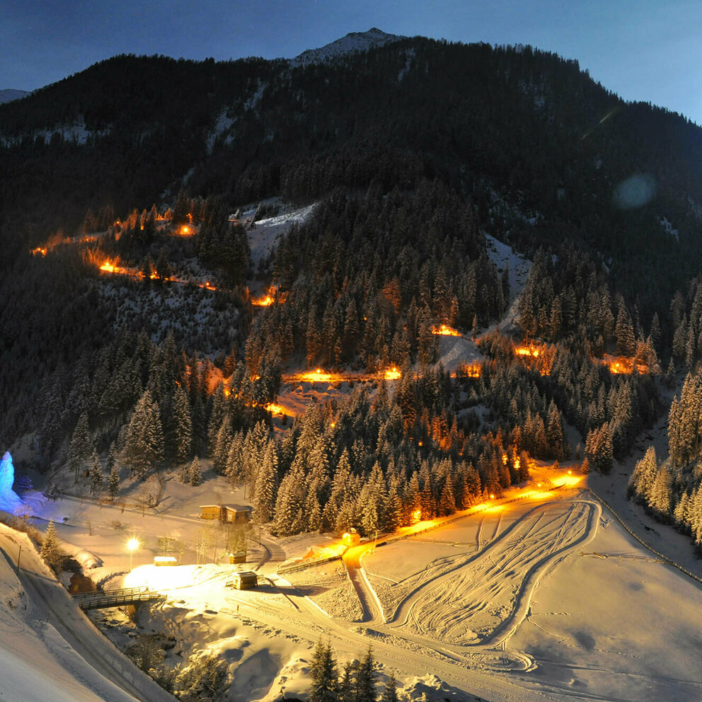 Rodelbahn Tilliachalmweg Die beleuchtete Rodelbahn Tilliachalmweg schlängelt sich in verschneiten Außervillgraten bei Nacht durch den Wald..