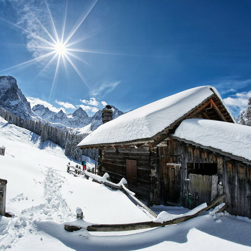 Eine tief verschneite Hütte in den sonnigen Dolomiten, blauer Himmel, weißer Schnee.