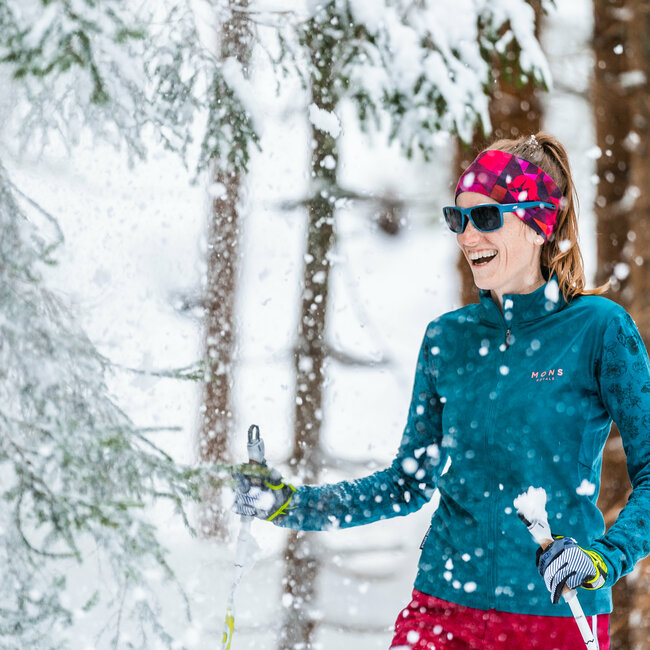 Eine Frau beim Langlaufen in Obertilliach steht lachend im verschneitem Wald.