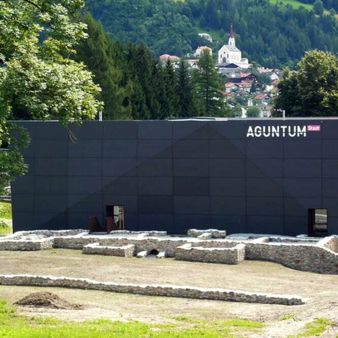 Aguntum Blick auf das Museum Aguntum in Dölsach, umgeben von römischen Ausgrabungen; im Hintergrund thront auf einer Anhöhe die Kirche von Dölsach