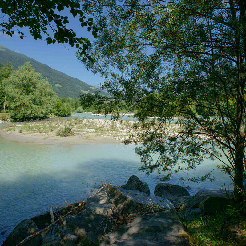 Untere Isel in Oberlienz Das türkis-blaue Wasser der unteren Isel in Oberlienz. In der Mitte ist eine kleine Sandbank. Am Ufer wachsen viele grüne Bäume.
