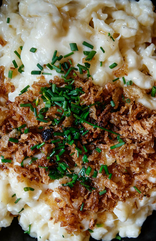 Kaesespatzle Käsespätzle mit gerösteten Zwiebeln traditionell in einem kleinen, schwarzen Eisenpfännchen