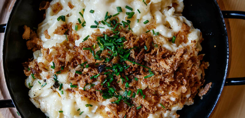 Kaesespatzle Käsespätzle mit gerösteten Zwiebeln traditionell in einem kleinen, schwarzen Eisenpfännchen