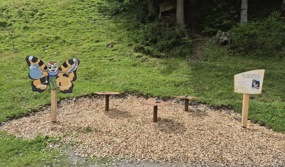 Ein Platz mit Holzspänen übersät mit einzelnen Spielstationen am "Weg der Sinne" in Virgen, Osttirol.