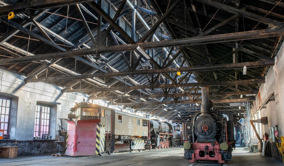 Innenansicht des Eisenbahnmuseums in Lienz. Im Vordergrund steht eine alte Lok sowie eine historische Wagengarnitur