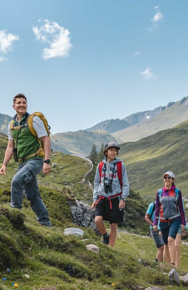 Mehrere Personen wandern durch den Nationalpark Hohe Tauern auf einer Rangertour mit Blick auf die Jagdhausalmen im Hintergrund.