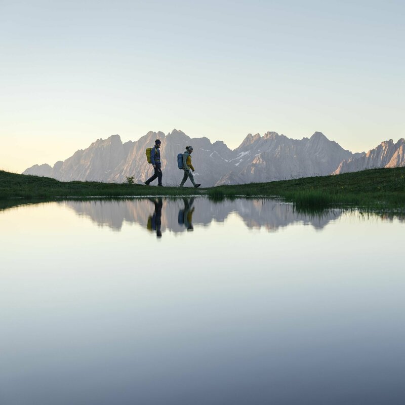 See bei der Sonnenaufgangstour Ein Paar wandert um einen See bei einer Sonnenaufgangstour, waehrend sich die Berge im See spiegeln.