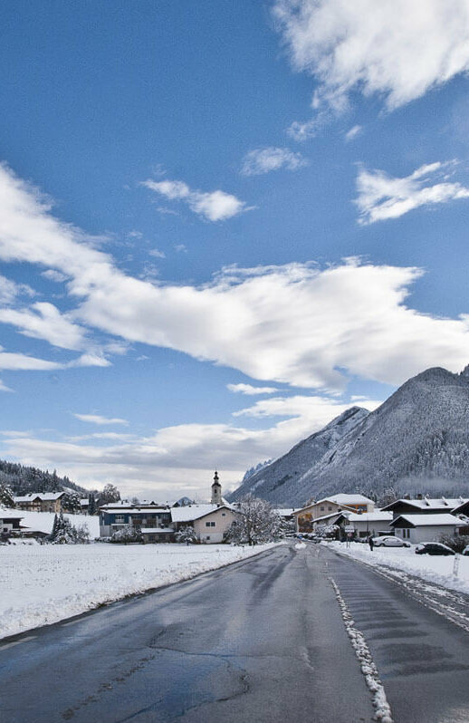 Abfaltersbach Winter Straße, die in den Ort Abfaltersbach führt, das schon im Hintergrund zu erkennen ist. Neben der Fahrbahn liegt Schnee.