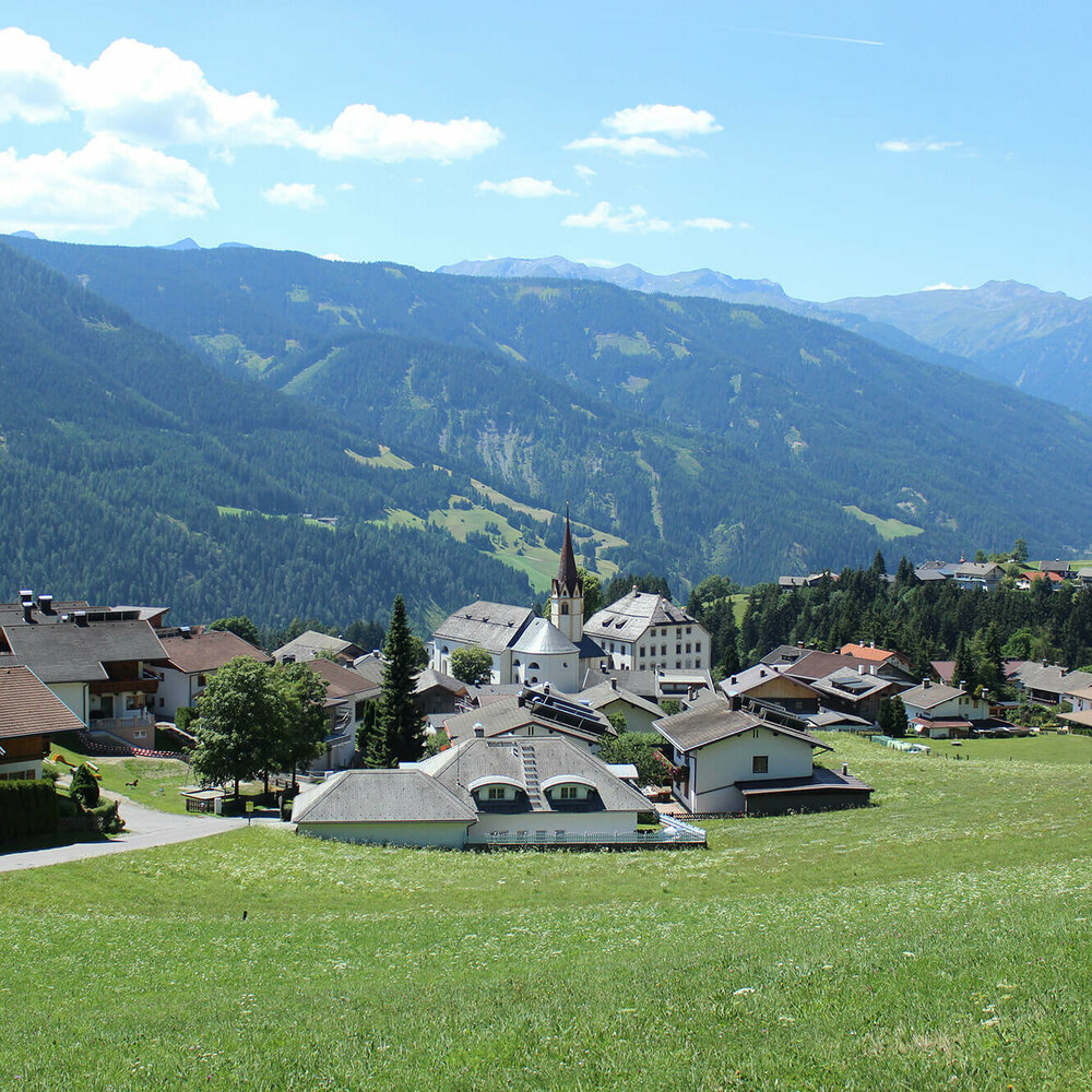 Anras Blick auf Anras mit einem grünem Feld im Vordergrund und bewaldeten Berghängen im Hintergrund.