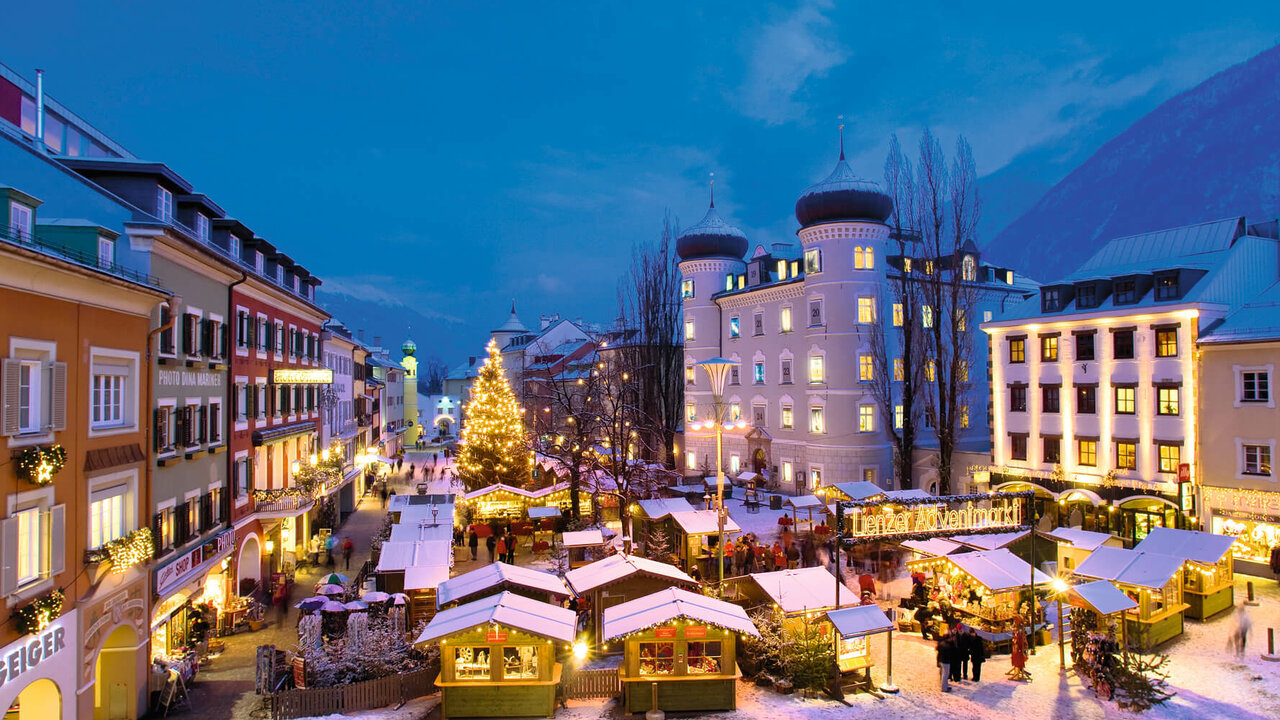 Adventmarkt Lienz Aufnahme vom Lienzer Adventmarkt am Hauptplatz bei Nacht. Die Hütten und ein großer Tannenbaum in der Mitte sind beleuchtet.