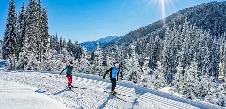 Langlaufen in Obertilliach Zwei Langläufer:innen genießen das Panorama der verschneiten Landschaft um die Langlaufloipe in Obertilliach.