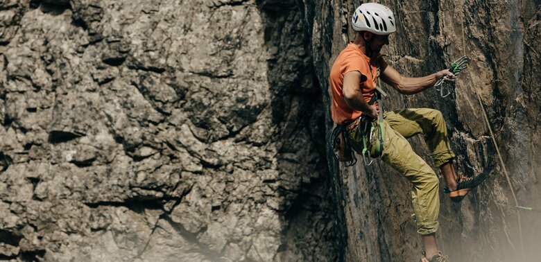 Laserz Klettersteig Ein Kletterer mit orangenem Shirt und weißem Helm, hängt an einer steilen Felswand am Laserz Klettersteig.