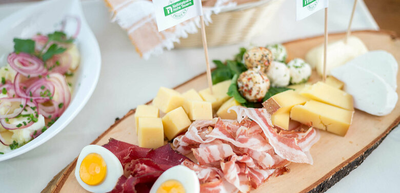 Regionsprodukte Brettljause mit verschiedenen Käsesorten in Würfel geschnitten, feinen Speck- und Henkelescheiben und hartgekochten Eiern.