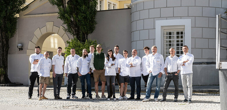 Teilnehmende Köche bei Osttirol de luxe in einer Reihe vor der Liebburg am Lienzer Hauptplatz aufgefädelt mit weißen Kochjacken und dunklen Hosen.
