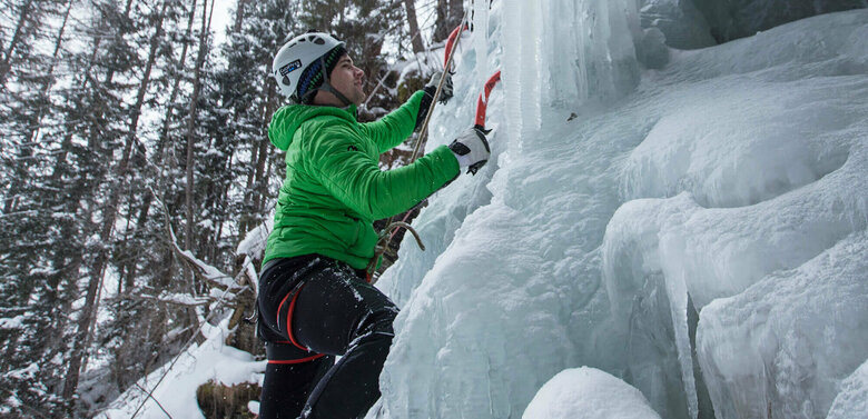 Eisfestival 2017 Eiskletterer in einer grünen Jacke, mit Pickel und Steigeisen auf einem zugefrorenen Wasserfall