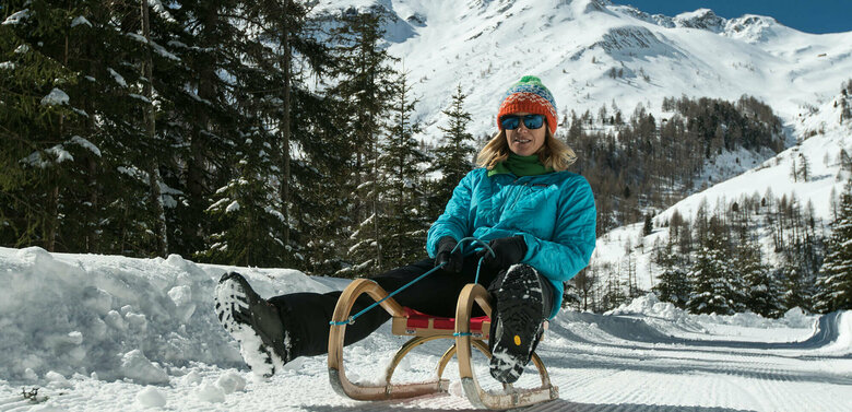 Rodeln in Osttirol Eine Frau mit blauer Jacke und bunter Mütze rodelt mit einem Schlitten ins Tal.