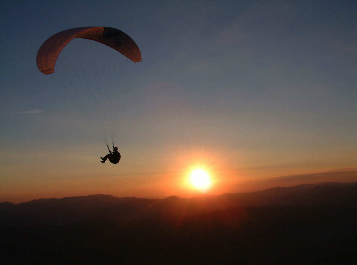 Paragleiten Paragleiter am abendlichen Himmel, dahinter Sonne, die bald am Horizont verschwindet.