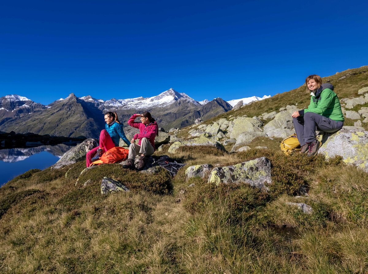 Rangertour Nationalpark Hohe Tauern Drei Frauen sitzen auf Felsen am Rande eines Sees im Nationalpark Hohe Tauern während einer Rangertour.