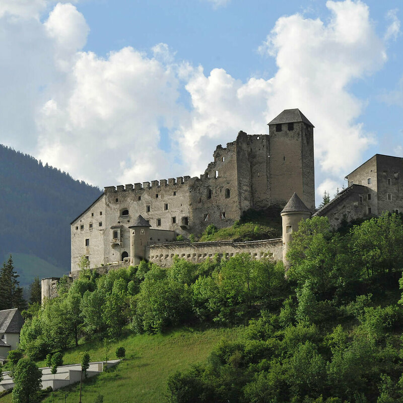 Burg Heinfels Majestätischer Sommerblick aus dem Tal auf die Burg Heinfels, eingebettet in grüne Laubbäume im satten Sommerkleid